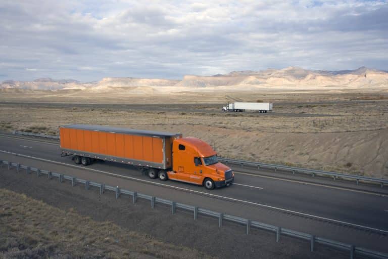 Orange tractor-trailer driving on highway with mountains in background