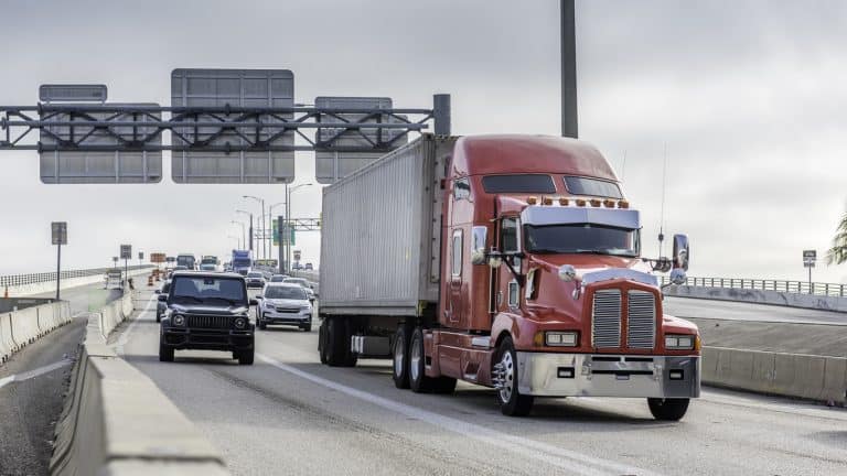 Tractor-trailer with red cab driving down highway